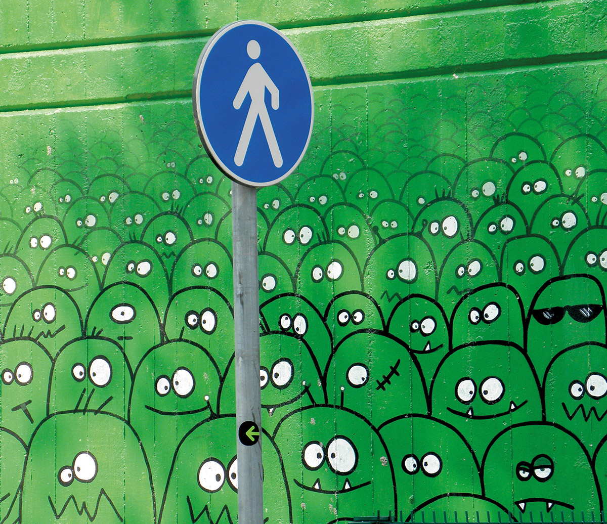 Wandbild mit lusitgen grünen Monsterköpfen davor ein Fußgängerschild.
